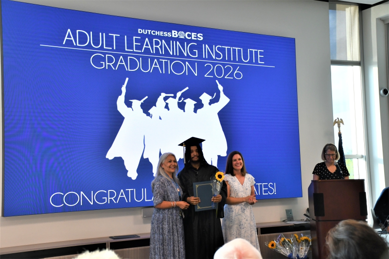 Graduate Ichidi Goulbourne poses with program caseworkers after receiving his certificate and sunflower.