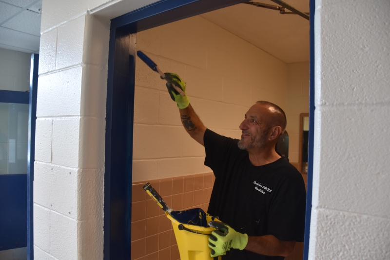 A member of the Facilities team paints a bathroom door frame at Salt Point Center with blue paint.