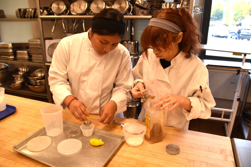 Culinary Arts and Restaurant Management students squeeze lemon and measure cinnamon for a recipe in the kitchen.