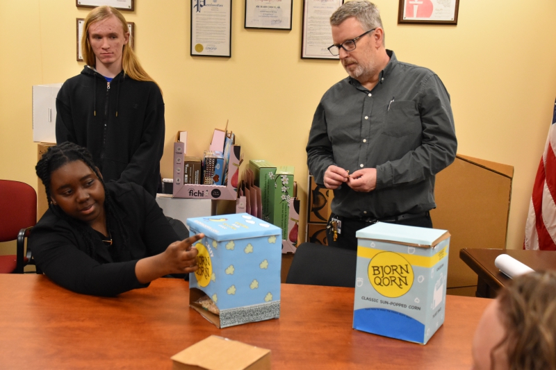 Graphic Design student Marree Bennett presents her BjornQorn box design for Viking Packaging staff as classmate Peter O'Connor and teacher Steve Lawson look on