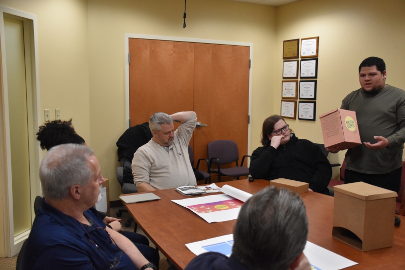 Graphic Design student Michael Ramos presents his BjornQorn box design to Viking Packaging staff who are sitting around a table in a conference room.